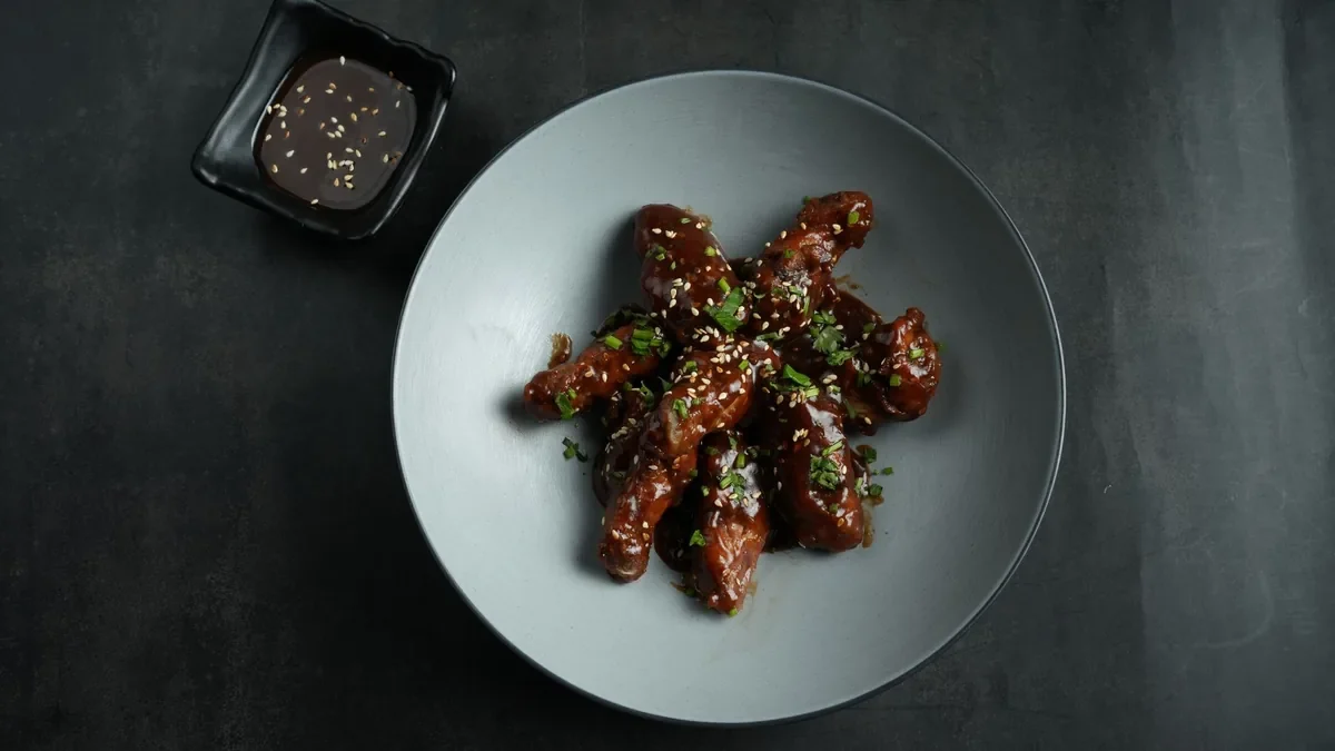 Chicken wings with a glazed sauce on a dark ceramic plate.