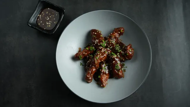 Chicken wings with a glazed sauce on a dark ceramic plate.