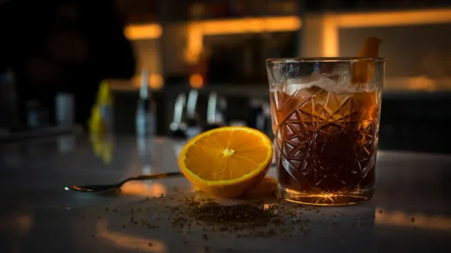A dark cocktail with orange peel on a bar counter.