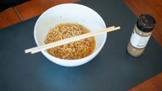 A bowl of noodles and chopsticks on a dark table.
