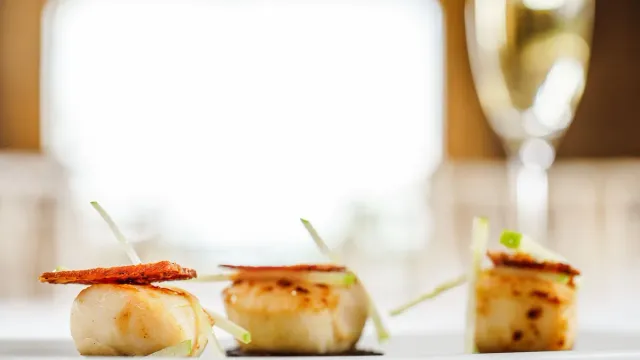 Seared scallops served on a pale plate.