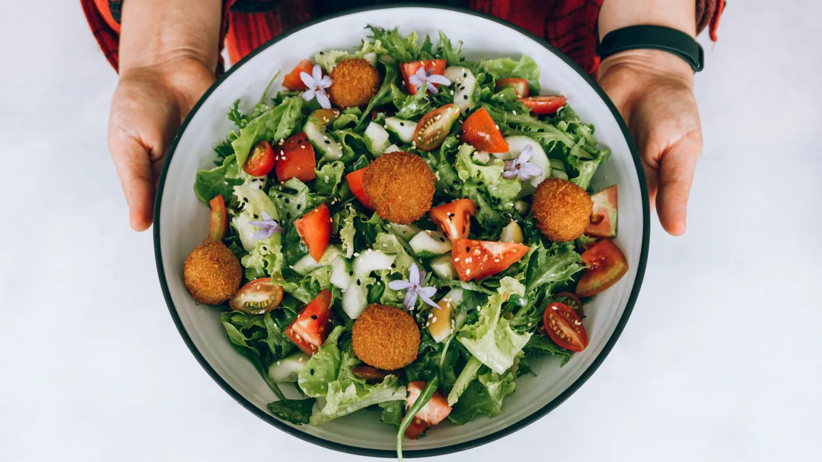 A vibrant overhead grain bowl with crisp greens, cherry tomatoes, avocado, chickpeas, and a light dressing drizzle in a clean ceramic bowl under bright side light.