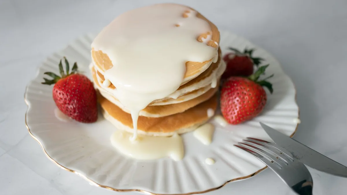 A stack of fluffy pancakes with dripping maple syrup and fresh berries on a marble counter in warm light.